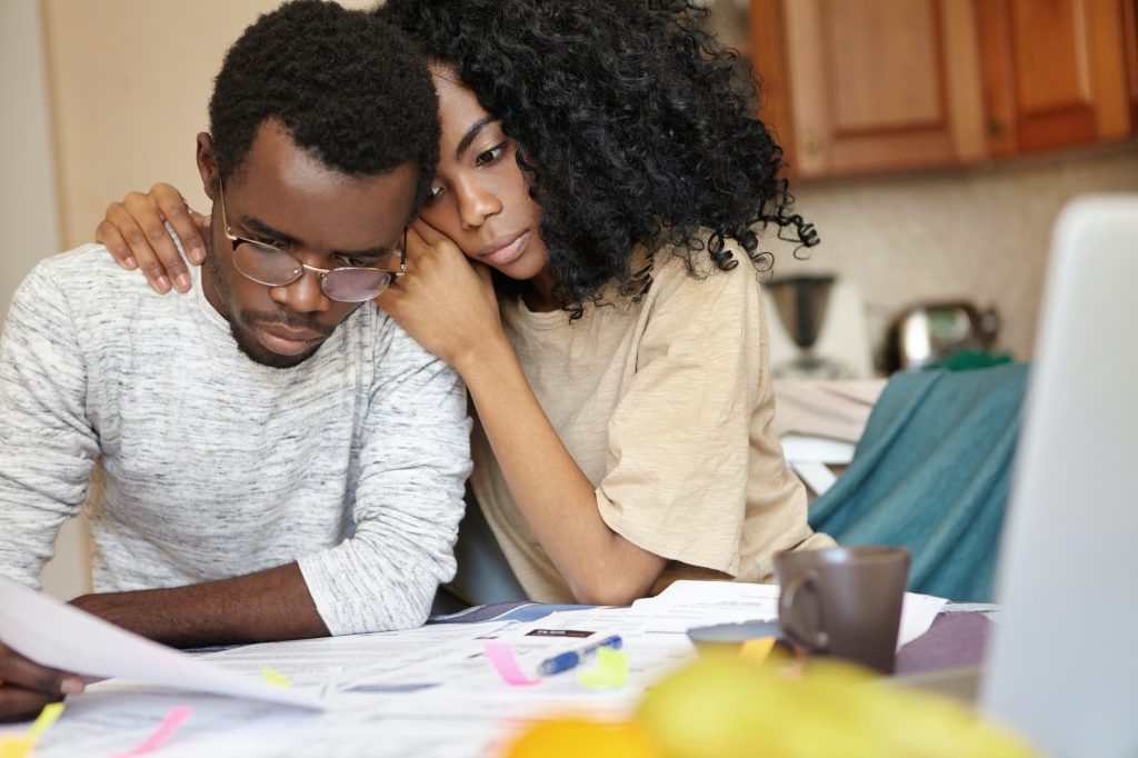 African couple is bankrupt. Sad male in glasses holding piece of paper feeling effortless to do some