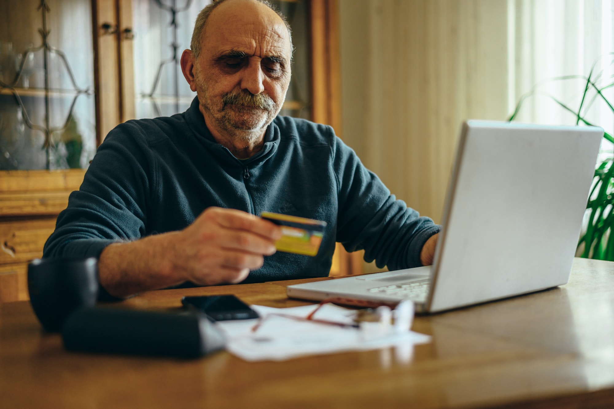 Senior man using a laptop and holding a credit card at home